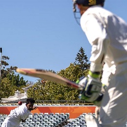 Two cricketers on an outdoor field. 一个在打保龄球，另一个拿着球棒准备击球.