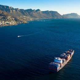 Aerial shot of a very large ship crossing 的 ocean with a mountain range in 的 background.