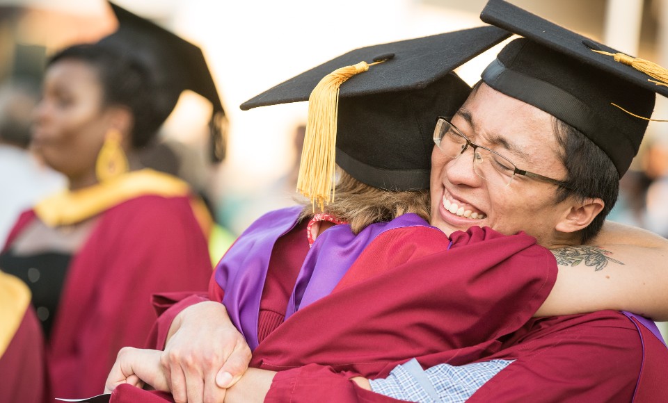 Male and female graduates hugging each other and smiling.