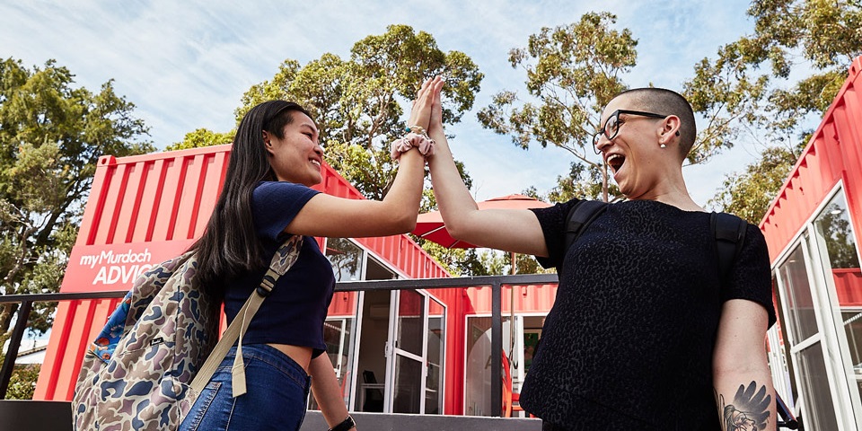 Two students laughing while high-fiving outdoors.