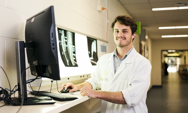 一个兽医站在电脑前，电脑侧面显示着x光片.