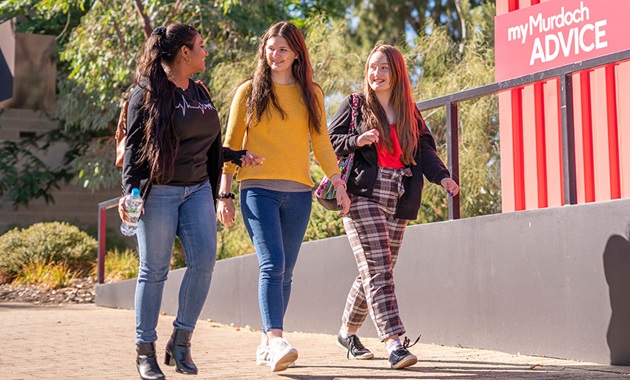 Three teenagers walking past a myMurdoch Advice hub at Murdoch's Perth campus