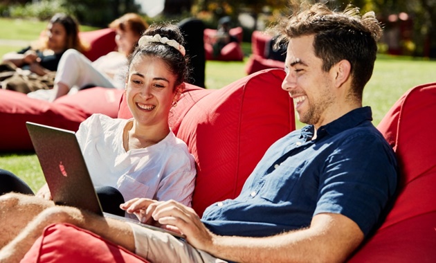 两个学生坐在布什庭院的豆袋里，微笑着看着笔记本电脑.