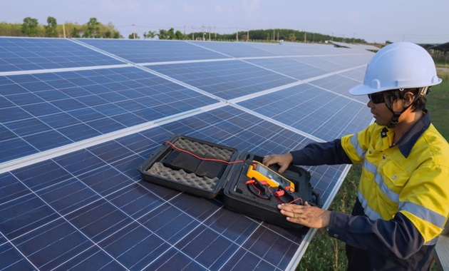 一名穿着高能见度衬衫和安全帽的男子正在太阳能电池板上工作.