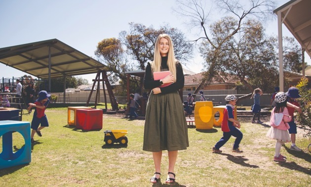 Primary school teacher standing in the playground surrounded by students