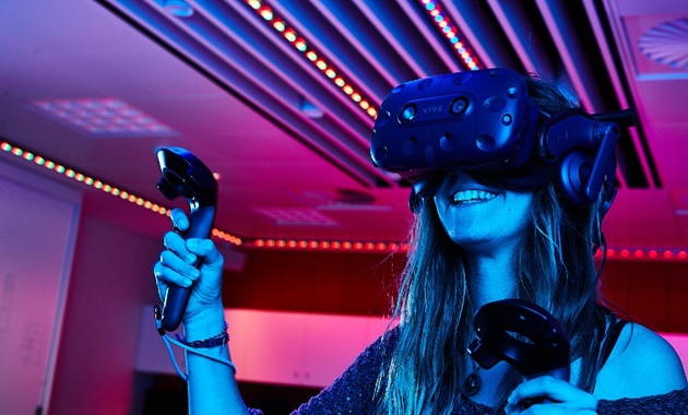 A female student wearing a VR headset and holding gaming controls.