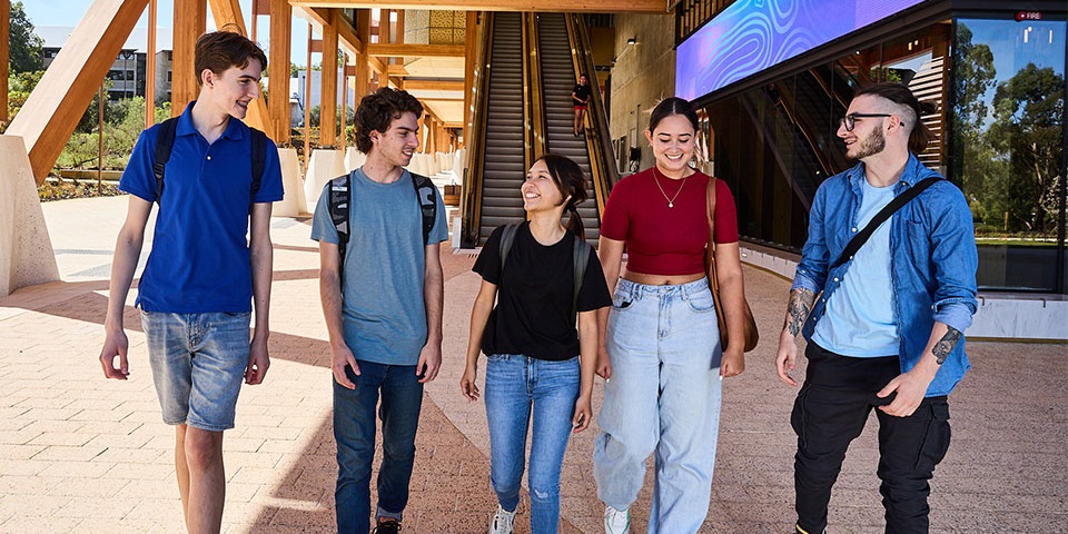 Five students walking together on a sidewalk, smiling and enjoying each other's company.