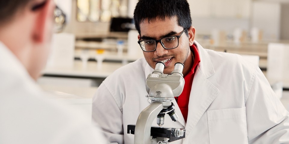 Male student in lab coat looking at microscope