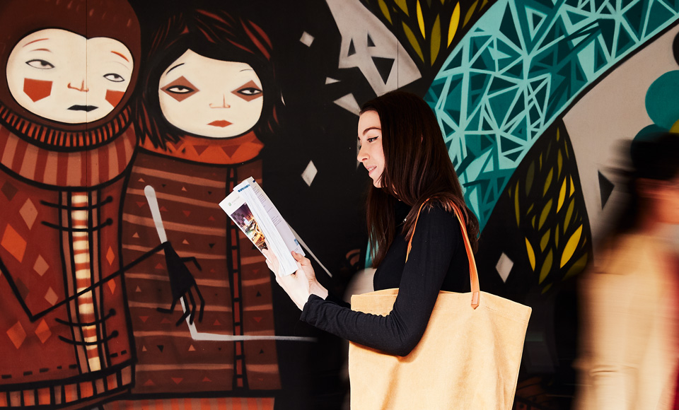 female student reading a book before a painted wall mural