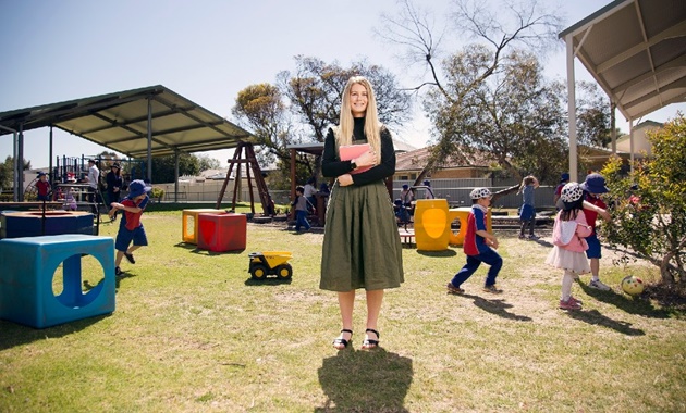 Primary teaching student in school playground with young pupils in background.