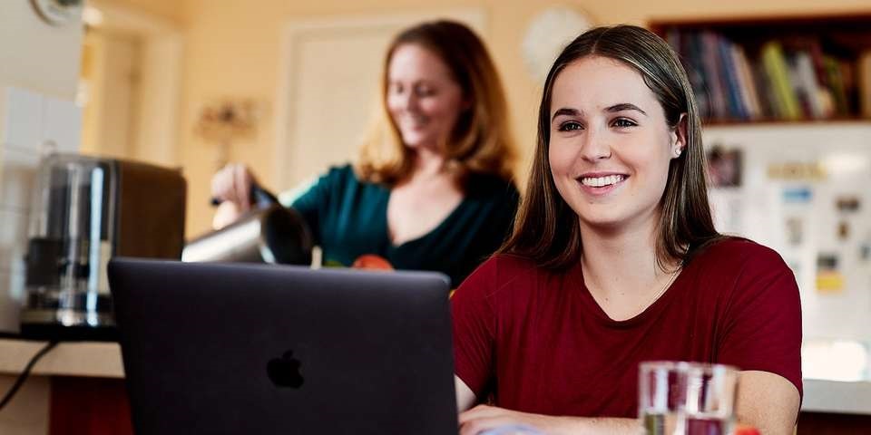 Woman in front of laptop and woman making coffee in the background