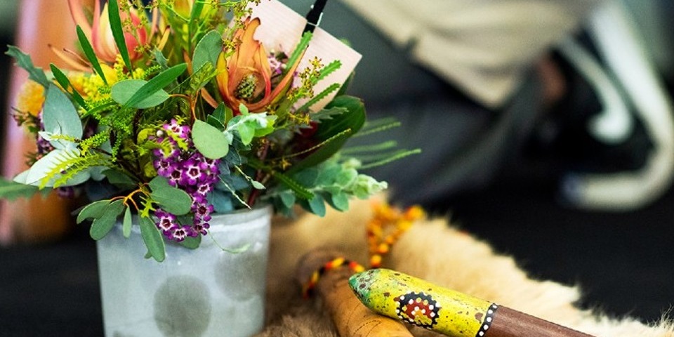 Indigenous clapsticks next to a vase full of bright, Australian native flowers.