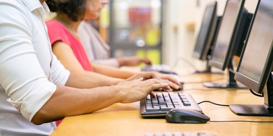 Three people sit, working at desktop computers.