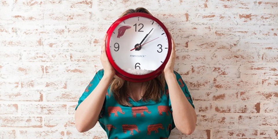 Woman in green dress holding up a red and white clock in front of her face.