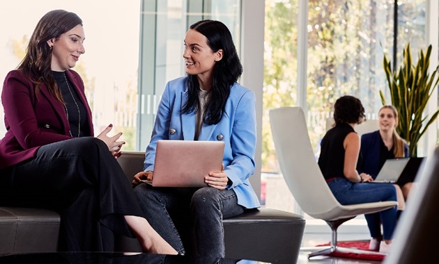 Two women sitting on a couch with a laptop having a business meeting