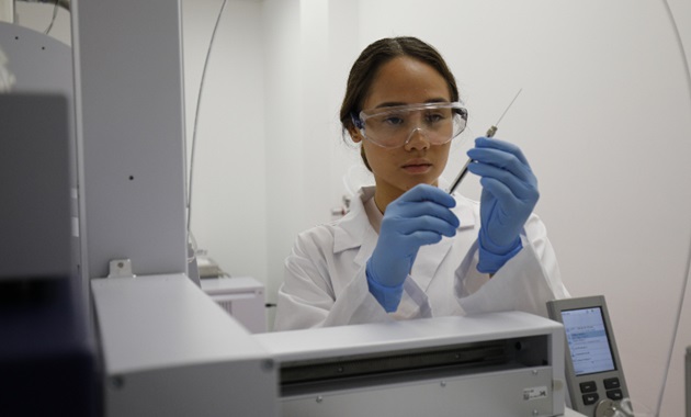 Female scientist wearing white lab coat taking sample from test tube with a syringe