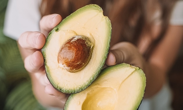 Girl holding halved avocado up to camera