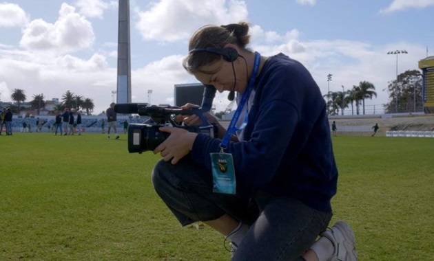 Student looks through video camera on a sports field