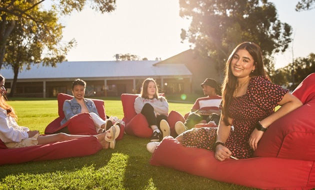 Girl turned to camera smiling, sitting among a group of students sitting on beanbags an grass