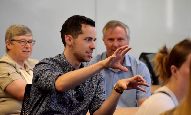 Student presenting to room in front of two people looking on