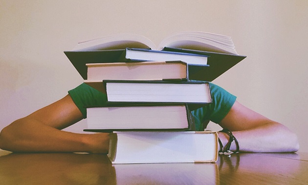 Student with head on hands behind pile of textbooks