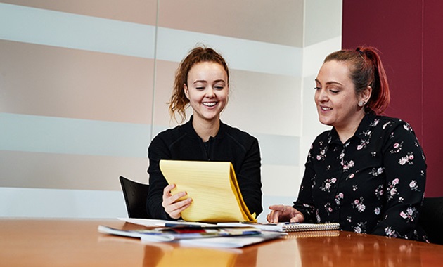 Two women look at a yellow legal pad.