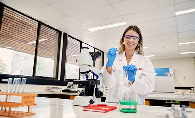 Female student in lab coat works in laboratory.