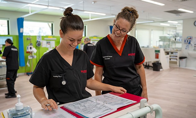 Female student looks over file with female tutor in the SimLab.