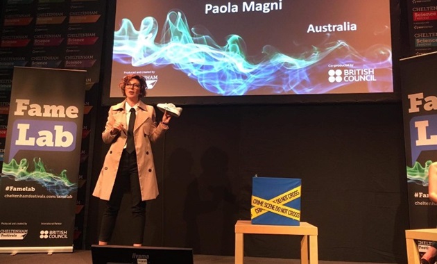 Paola Magni holding a shoe performing at the International FameLab finals 2019