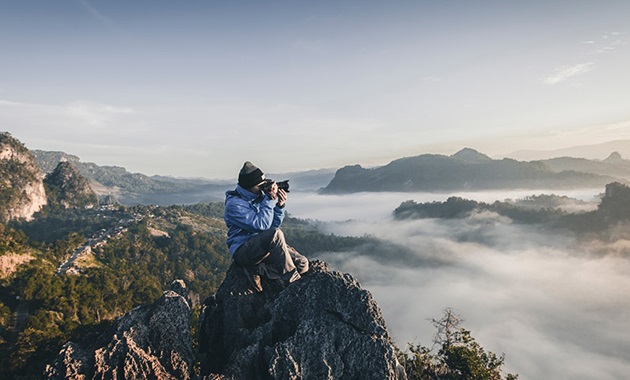 Man taking a photo at the top of a misty mountain range