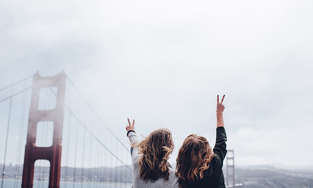 Two girls waving their hand in the air in front of bridge