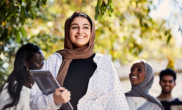 Female student wearing hijab smiling and holding laptop.