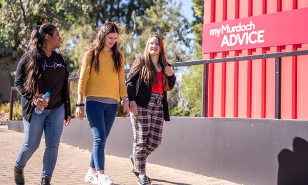 Three students walking near an advice hub