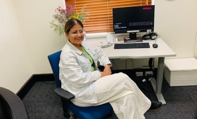 Student in lab coat sits in front of computer smiling