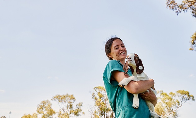 Female student holding a small goat, smiling.