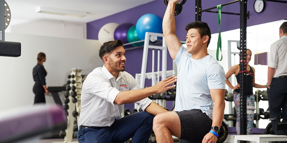 Chiro student helping person using weights in gym