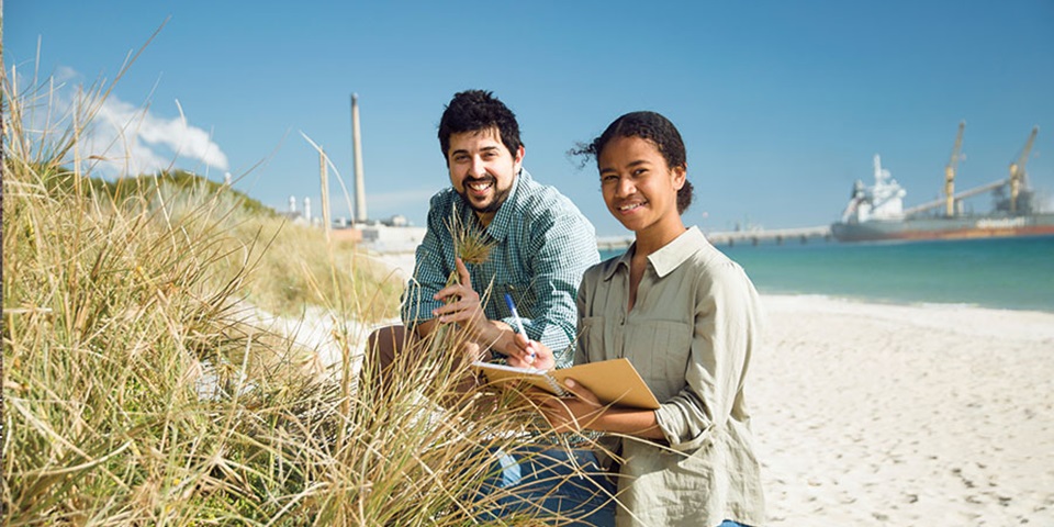 2 students on beach collecting samples